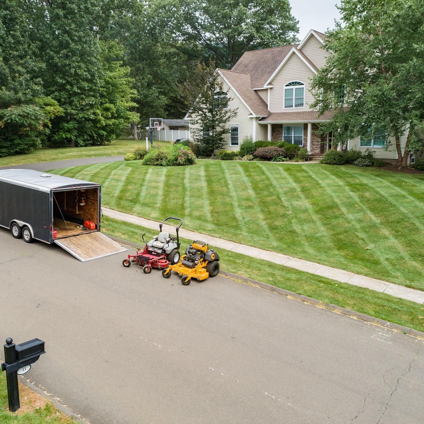Lawn care equipment outside a home with freshly mowed grass and a trailer parked nearby.