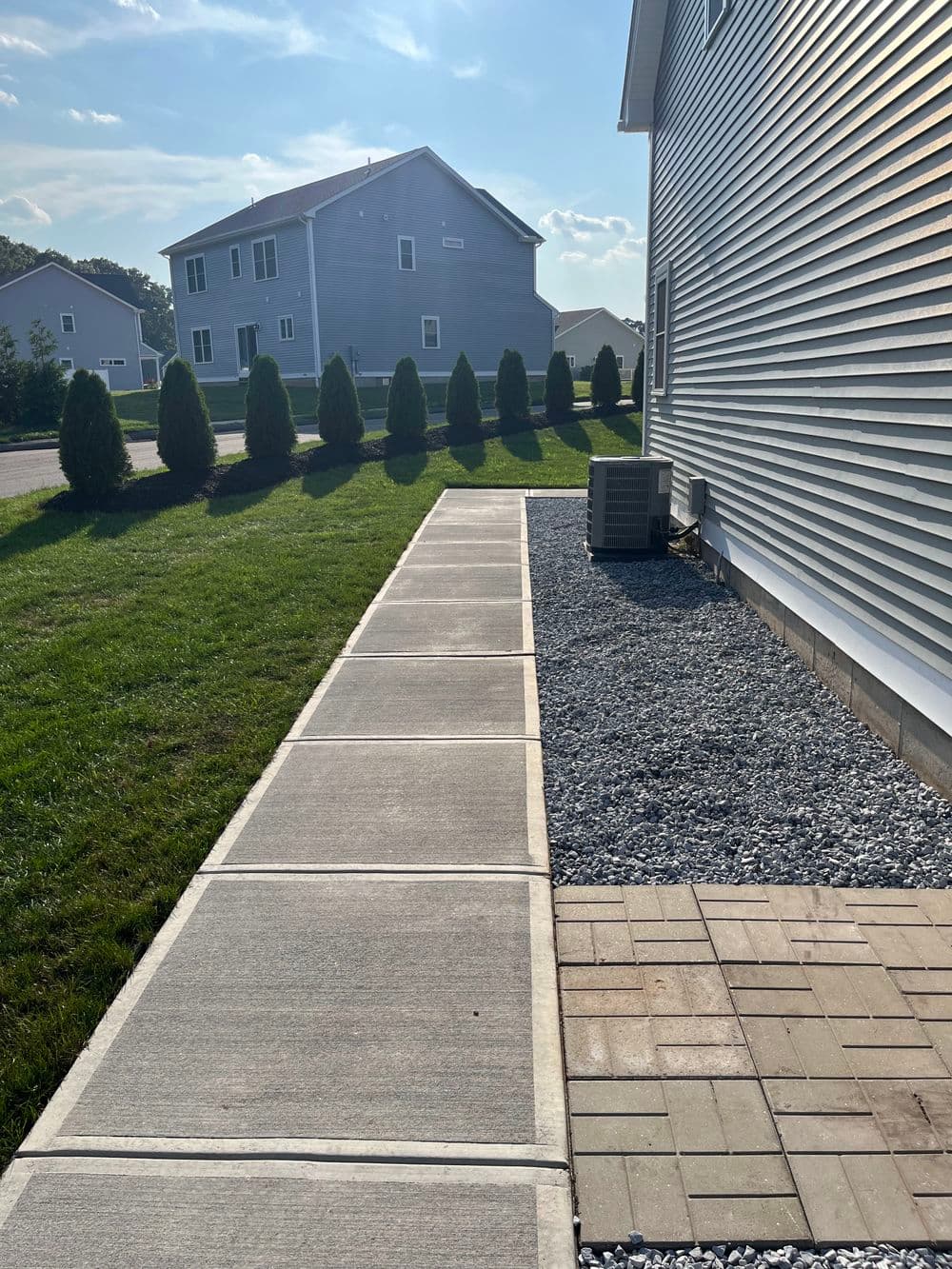 Sidewalk leading to a residential home, flanked by neatly trimmed shrubs and gravel.