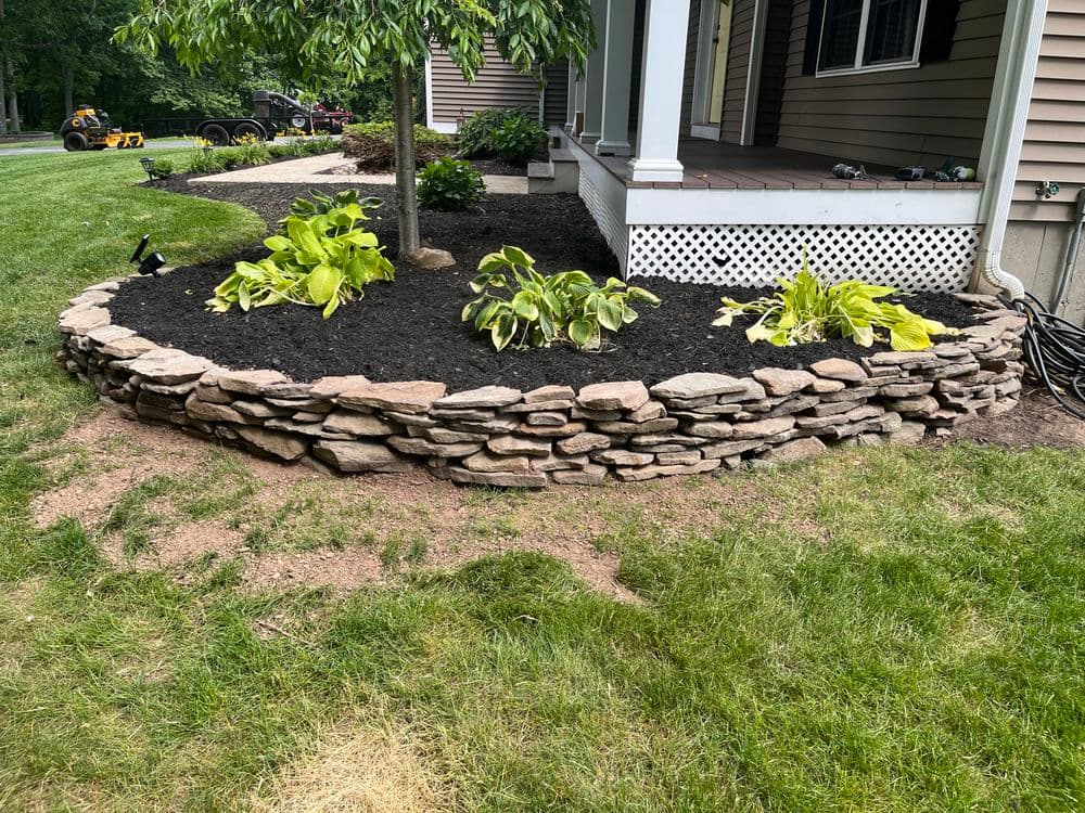 Stone wall garden bed with lush plants and mulch in residential landscaping.