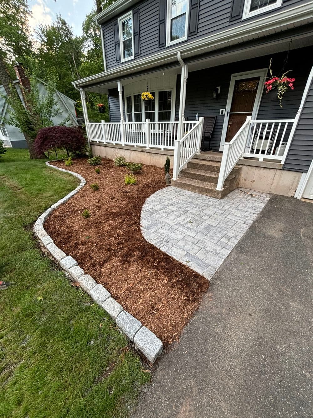 Newly landscaped home entrance with a stone walkway, flower beds, and mulched garden area.