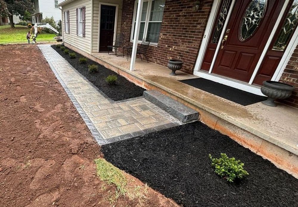 Newly landscaped front yard featuring paver walkway, black mulch, and trimmed shrubs.